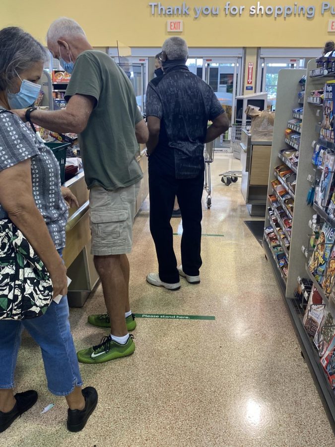 People are standing in line waiting to pay for their items. They aren’t following the guidelines Publix put in for social distancing, but they are wearing masks. 

