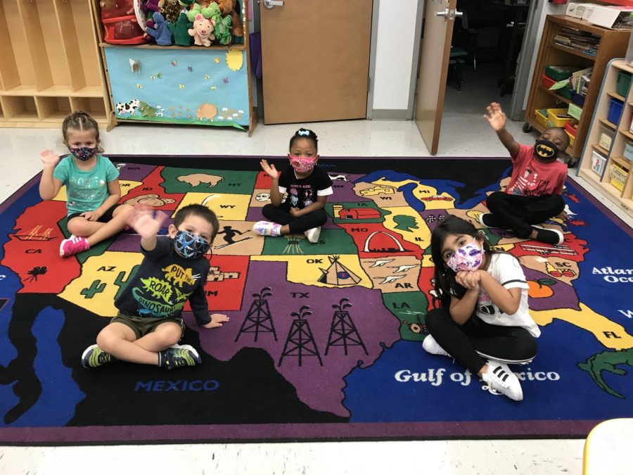 The preschoolers at the Little Broward Learning Lab sit and wave on the carpet, socially distant and with their batman, tie-dye, and floral patterned masks on.