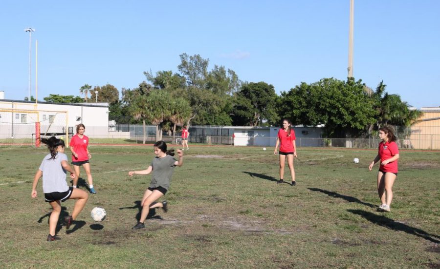 Five girls from the soccer team practicing there passing and pressuring at there home field.