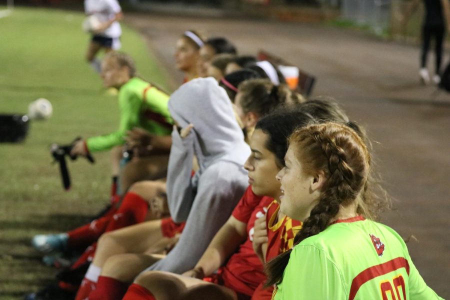 The girls on the sidelines watch as their teammates play in the game.