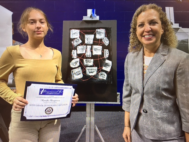 10th grader Kamilla Alasgrova at the 2023 Congressional Arts Competition. She stands infront of her work next to Congresswoman debbie Wasserman Schultz. She has just won the honorable mention for 10th grade.