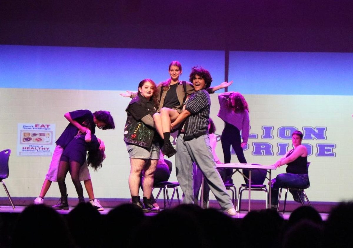 Noa Heby as Janis Ian, Cj Clemons as Cady Heron, and Noah Alejo as Damian Leigh, all onstage performing to the audience a Mean Girls school musical.