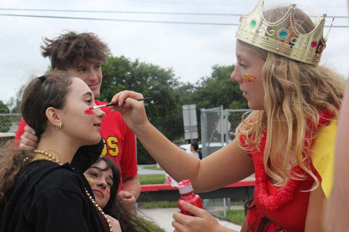 Athena Hawn doing face paint on ______ to show some school spirit of red and gold. 