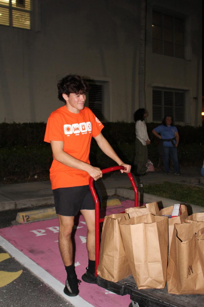 Blake Higgs, a senior at SBHS, aids with the cart full of bags for the other volunteers to distribute bags containing food and household necessities to the families.