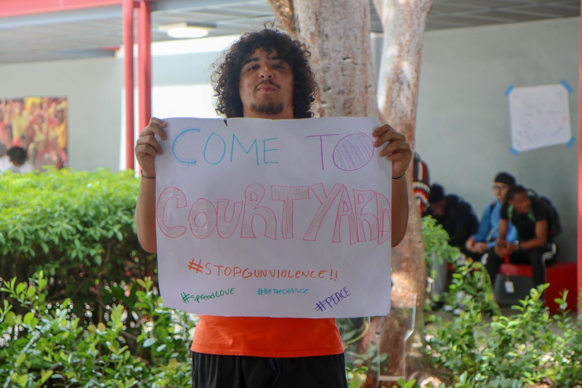 Senior Javiar Montes makes his way around school campus holding a sign inviting students to the courtyard for activities aimed to raising awareness and taking a stand against gun violence.